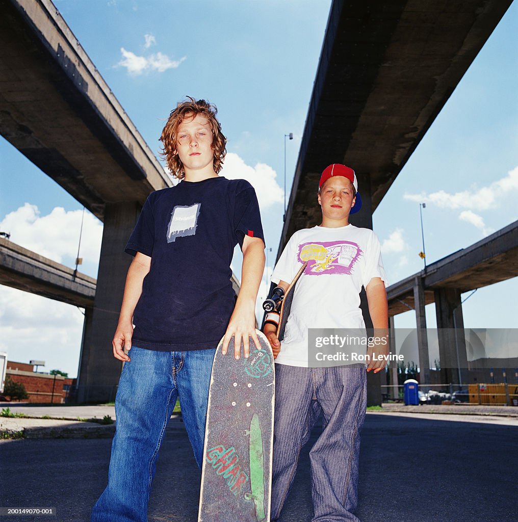 Two teenage boys (12-14) under highway with skateboards, portrait