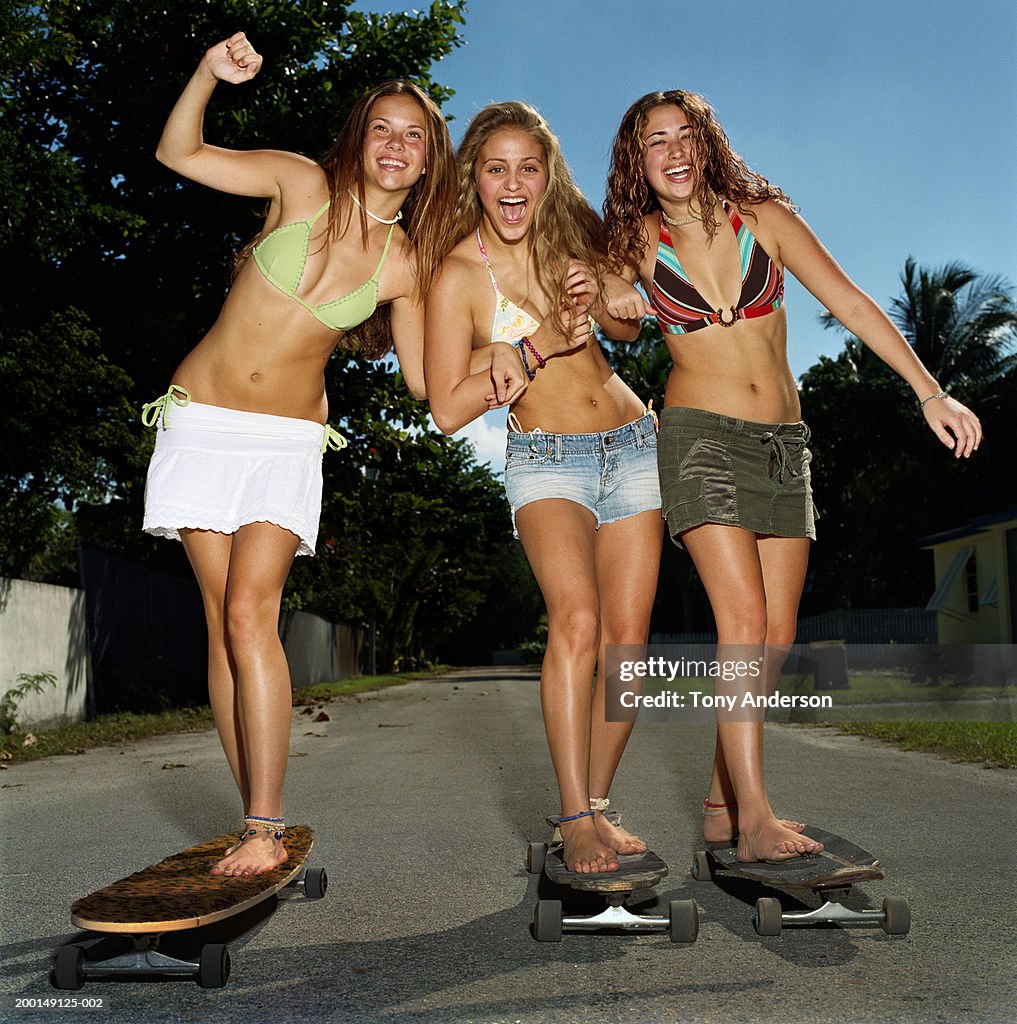 Three teenage girls (16-18) standing on skateboards, smiling, portrait
