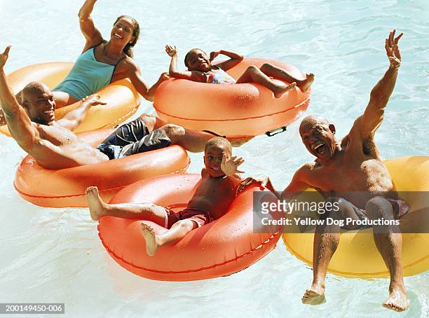family on plastic tube in swimming pool, smiling - bermuda shorts stock pictures, royalty-free photos & images