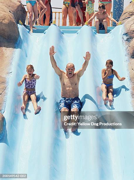 grandfather with grandaughters (8-10) sliding down water ride - water slide stock pictures, royalty-free photos & images