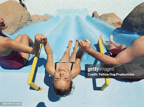 girl (8-10) holding parents hands going down water slide, portrait - tobogán de agua fotografías e imágenes de stock