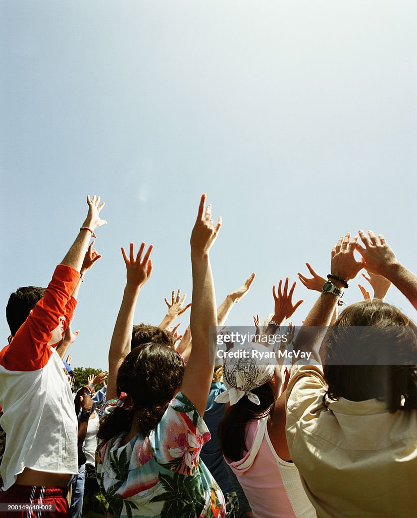 Crowd of young adults at outdoor concert, raising hands in the air
