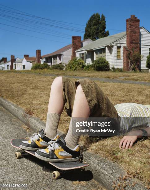 teenage boy (13-15) with skateboard lying on his back by sidewalk curb - teen boy shorts imagens e fotografias de stock