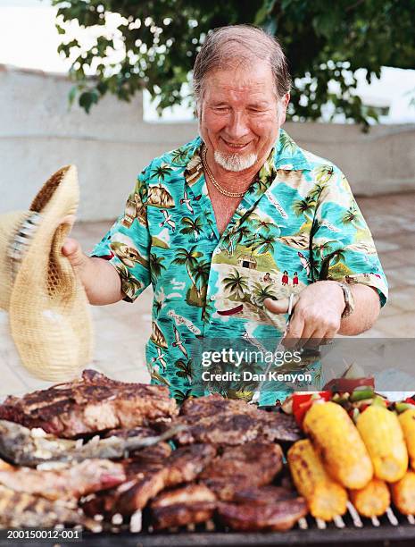 mature man tending to barbecue - grillzange stock-fotos und bilder