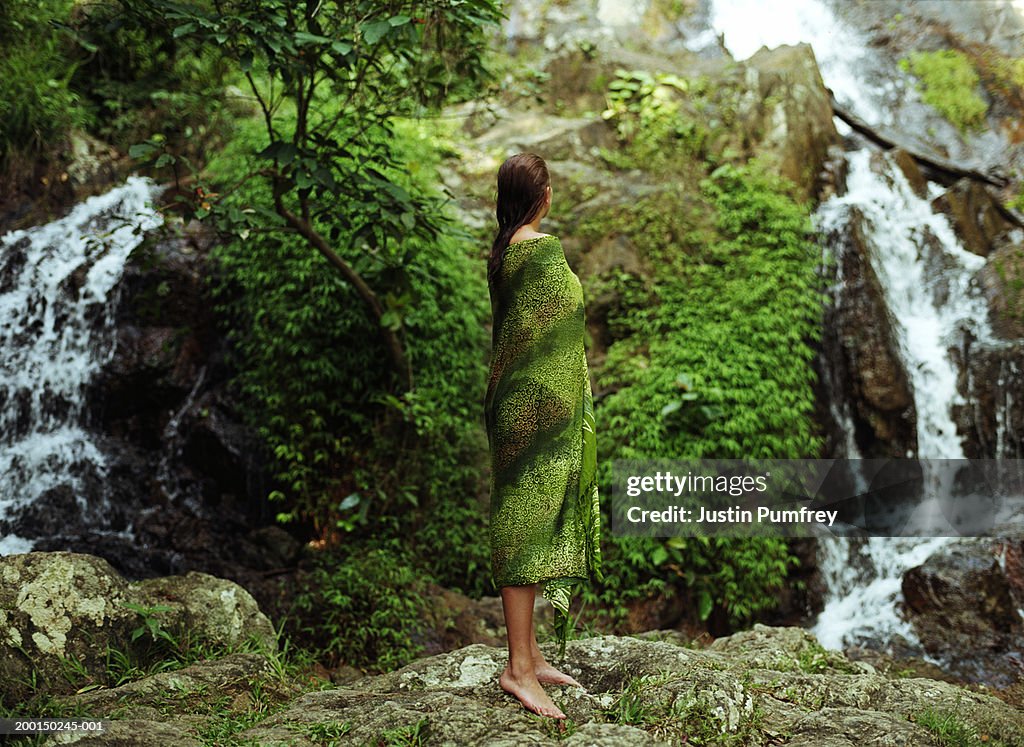 Woman by waterfall, wrapped in sarong, rear view