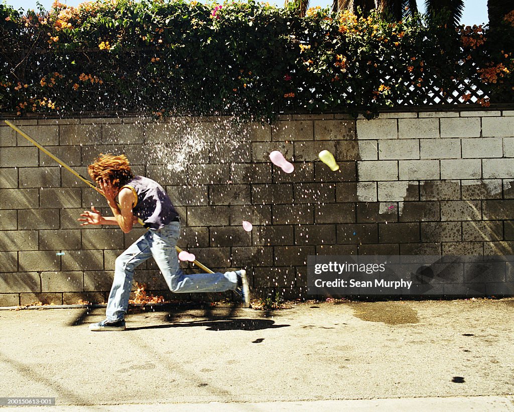 Boy (13-15) in water fight, running from water balloons