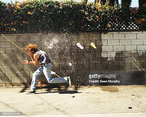 boy (13-15) in water fight, running from water balloons - boy jeans stockfoto's en -beelden