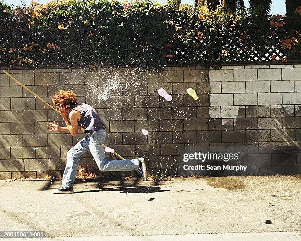 boy (13-15) in water fight, running from water balloons - boy jeans stock pictures, royalty-free photos & images