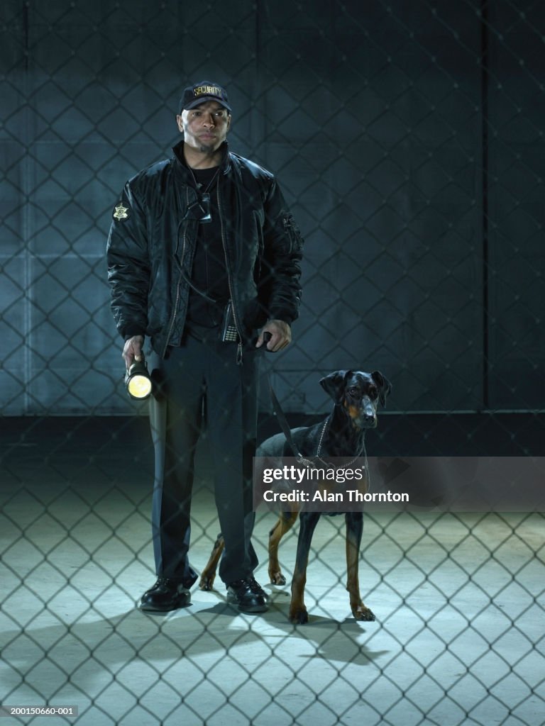 Security guard with dog and torch, view through chain link fence