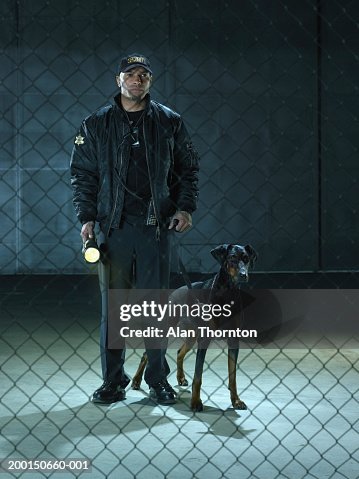 Security guard with dog and torch, view through chain link fence Security guard with dog and torch, view through chain link fence