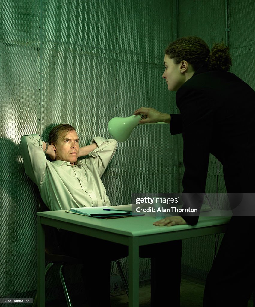 Woman shining angle poise lamp into man's face