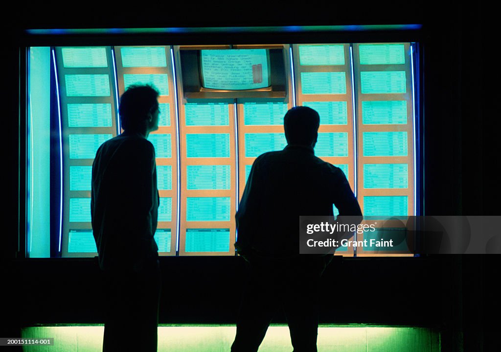 Man and teenage boy (15-17) looking at stock market displays, evening