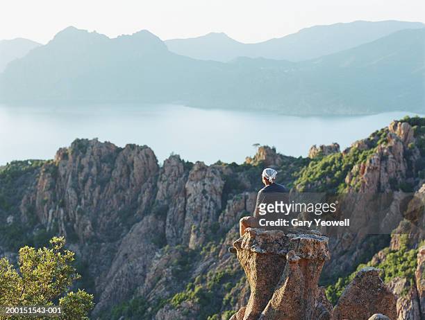 man sitting on rock overlooking sea and mountains, rear view - corse fotografías e imágenes de stock