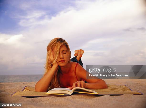 young woman lying on beach , reading book - beach mat stock pictures, royalty-free photos & images