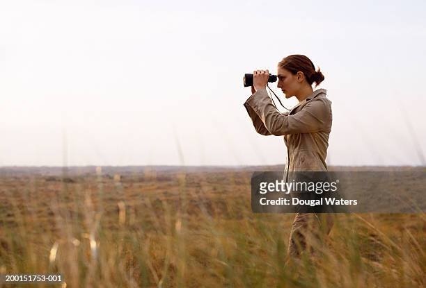 young woman looking through binoculars outdoors, side view - safari stockfoto's en -beelden
