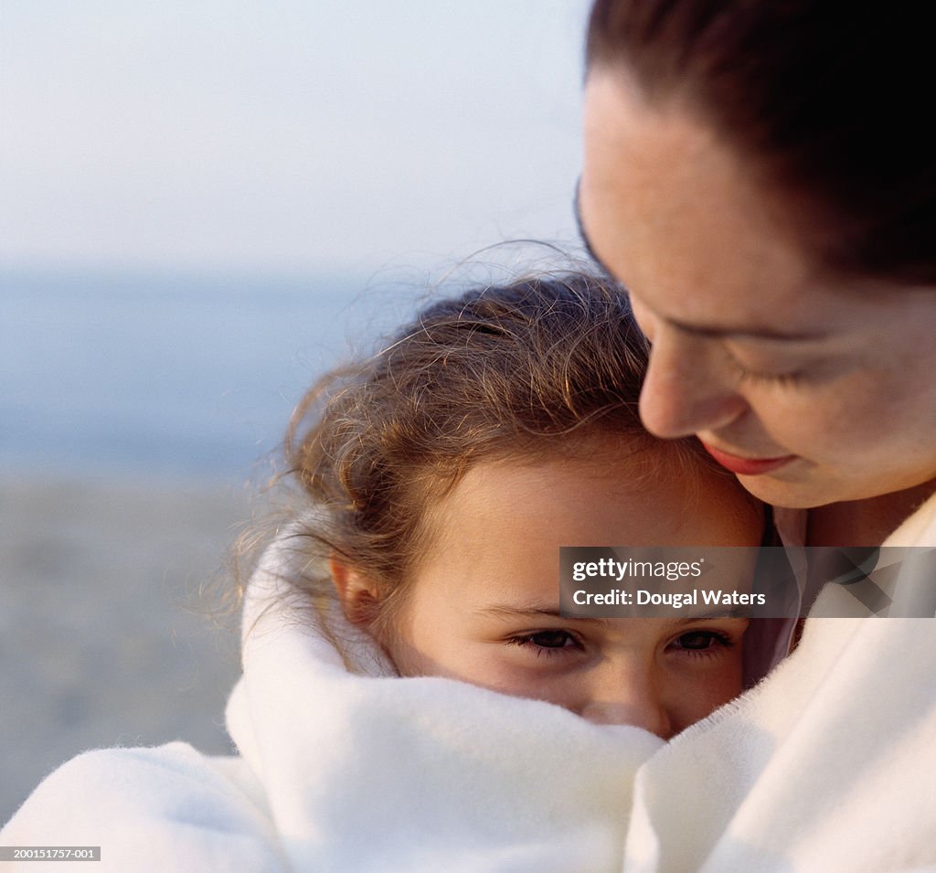 Woman and girl (6-8) embracing outdoors, close up