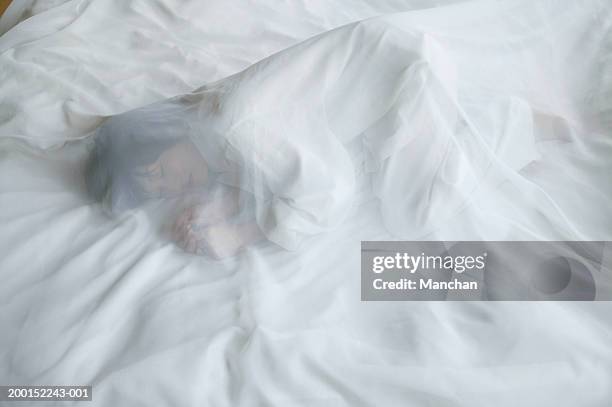 woman lying on bed, under transparent sheet - foetushouding stockfoto's en -beelden