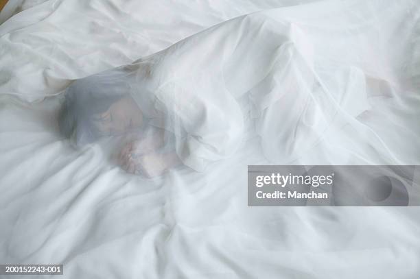 woman lying on bed, under transparent sheet - woman curled up stock pictures, royalty-free photos & images