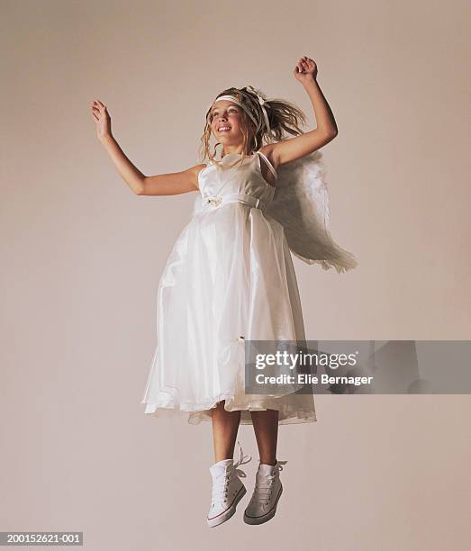 young girl (7-9) dressed as angel jumping, arms raised, smiling - angel white dress stock pictures, royalty-free photos & images