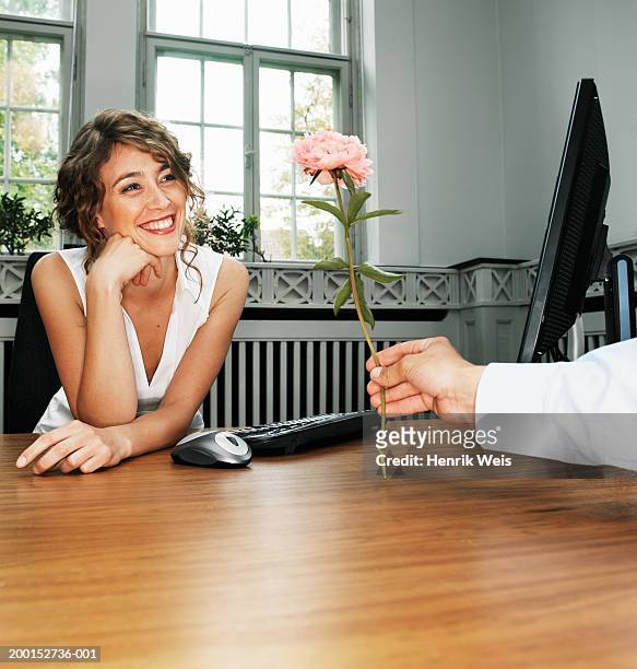 man passing flower to woman at desk with computer, smiling - passing giving photos et images de collection