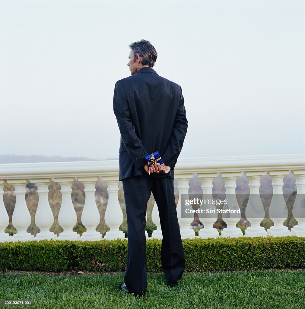 Man holding present, standing in yard, rear view