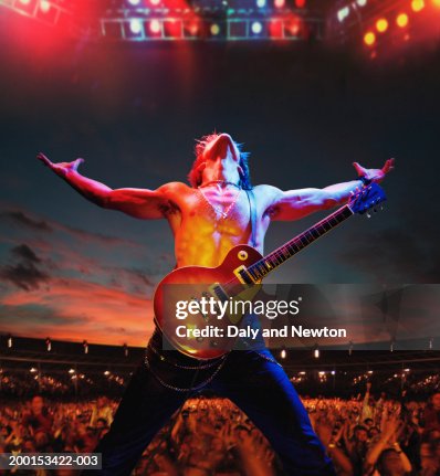 Bare chested man with guitar on stage by crowd, arms outstretched Bare chested man with guitar on stage by crowd, arms outstretched