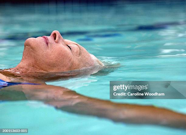 senior woman floating in pool, eyes closed, side view - alte frau badeanzug stock-fotos und bilder