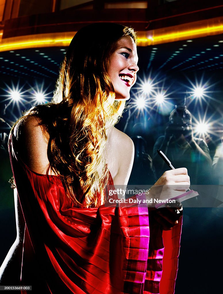 Young woman signing autograph, crowd taking photos in background