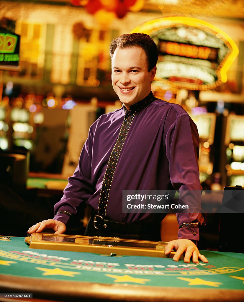 Dealer standing behind poker table in casino, portrait