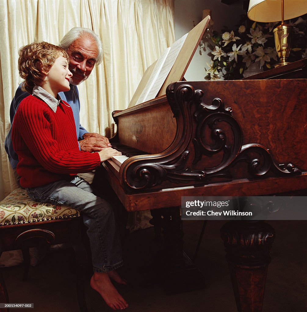 Boy (6-8) and grandfather playing the piano, smiling, side view