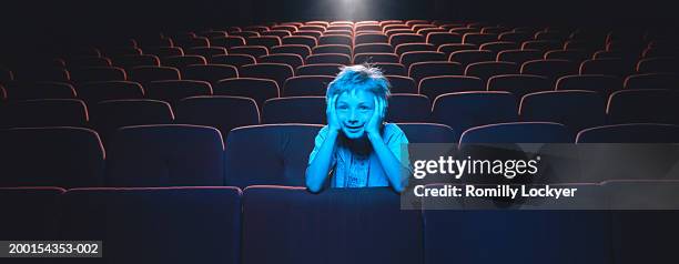 boy (6-8) leaning on auditorium seat, illuminated by light - kinosaal stock-fotos und bilder