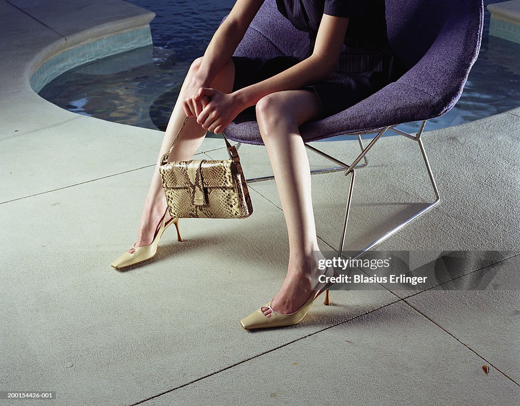 Woman on chair holding handbag near pool