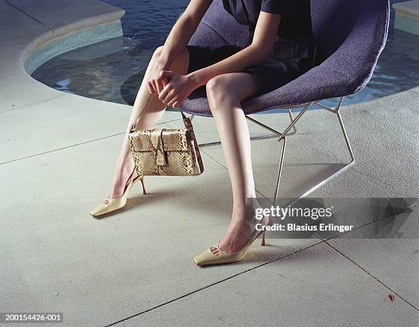 woman on chair holding handbag near pool - accessory foto e immagini stock