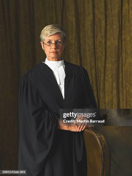 senior female judge standing by leather chair, portrait - ceremonieel gewaad stockfoto's en -beelden