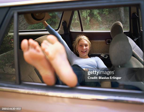 teenage girl (15-17) lying in car, smiling, portrait - girl barefoot stock-fotos und bilder