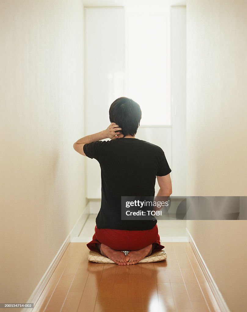 Man Kneeling On Cushion In Hallway Rear View High-Res Stock Photo