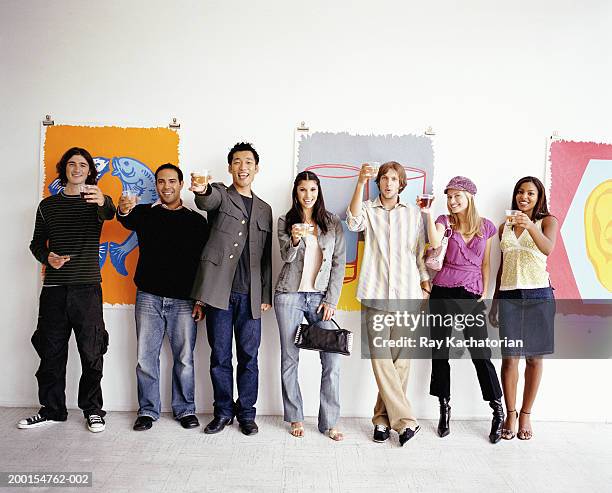 young adults standing against wall in art gallery, holding up drinks - vernissage stock-fotos und bilder