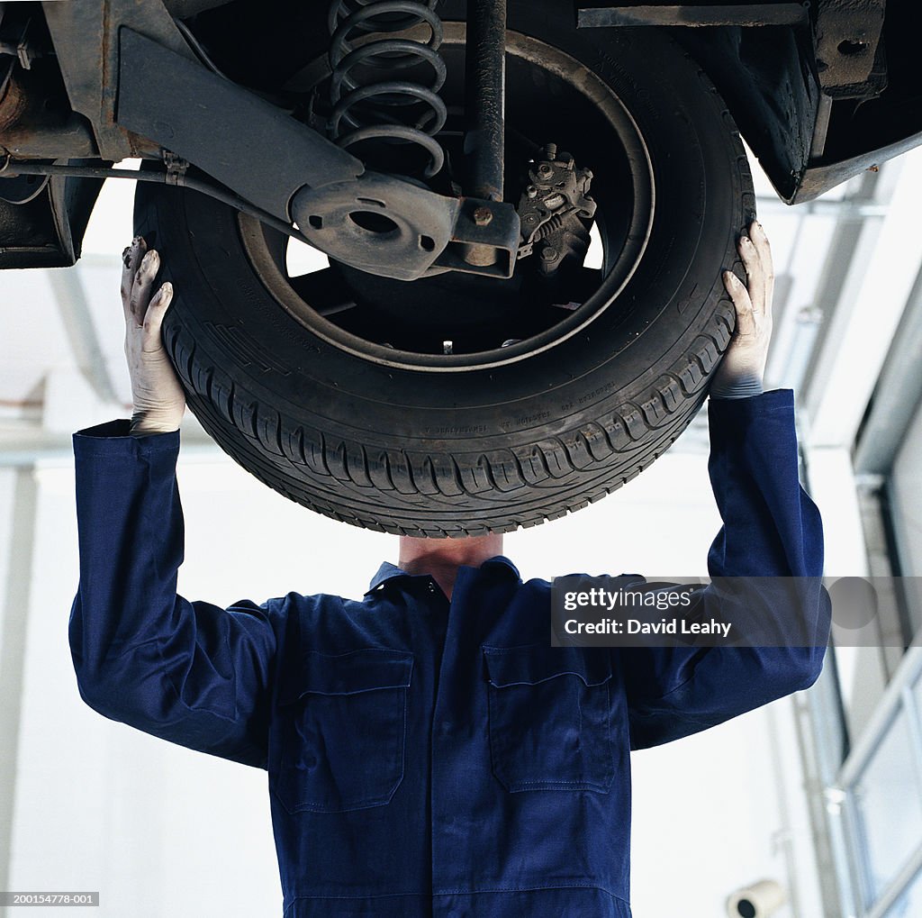Mechanic working on car, face obscured by wheel, low angle view