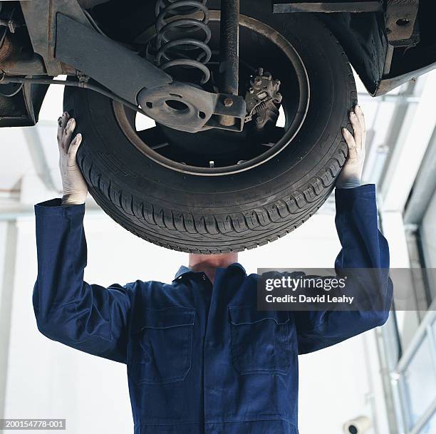 mechanic working on car, face obscured by wheel, low angle view - blue jumpsuit bildbanksfoton och bilder