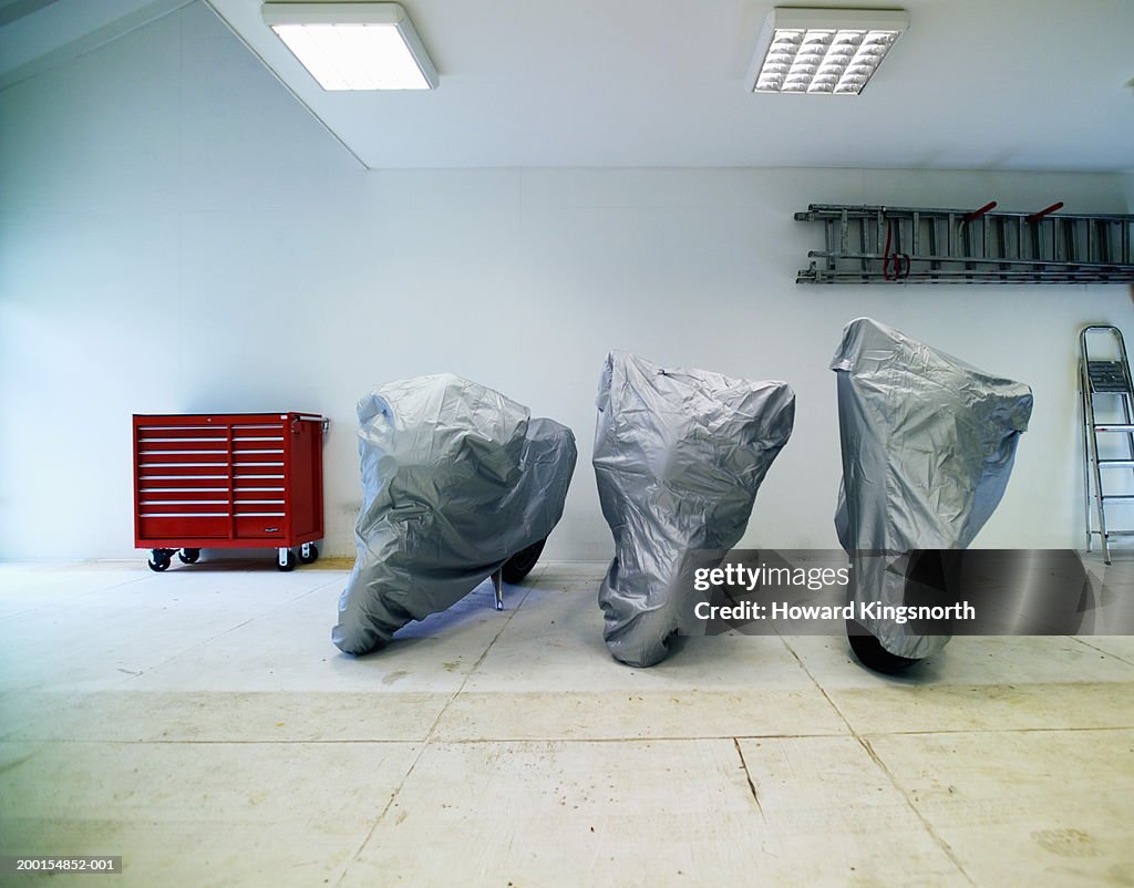 Three motorbikes in garage under protection covers