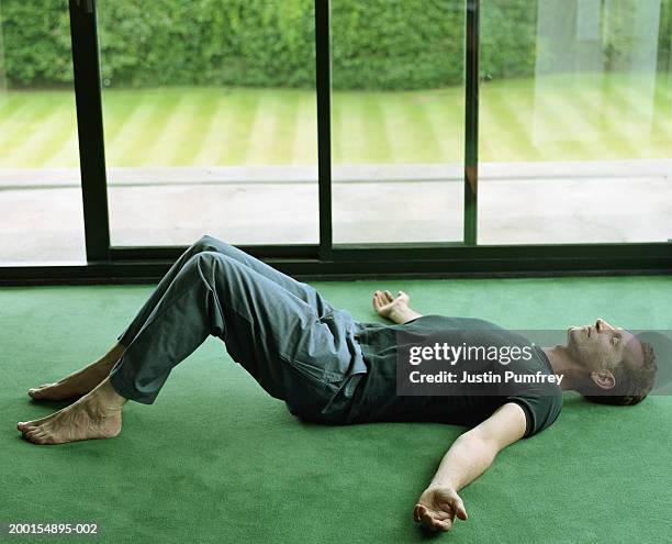 mature man lying on floor by large window, arms outstretched - supino foto e immagini stock