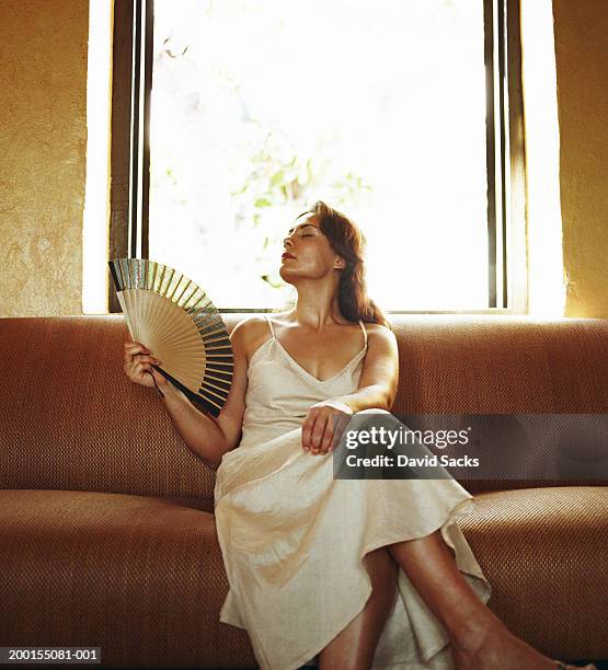 woman holding fan on sofa - hand fan stock pictures, royalty-free photos & images