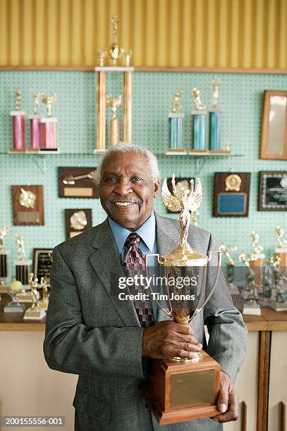 senior man standing by awards display, holding trophy - trophy display stock pictures, royalty-free photos & images