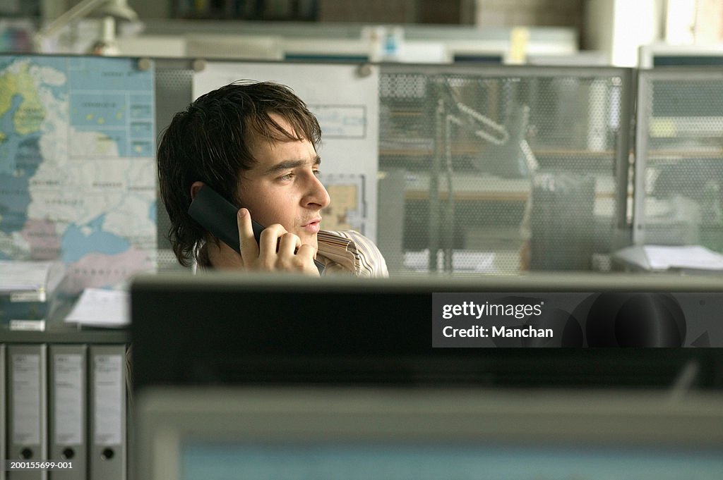 Male office worker sitting at desk, using telephone