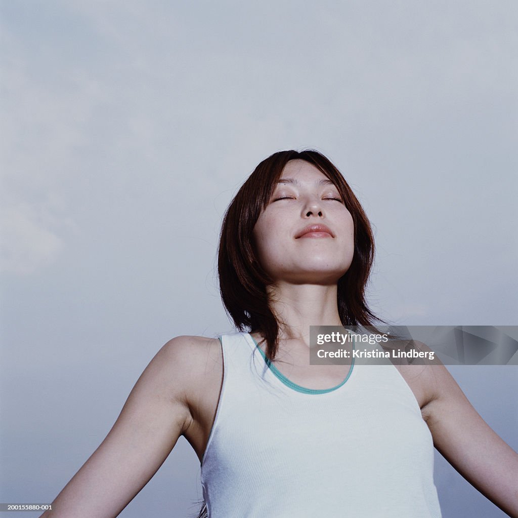 Young woman  with arms outstretched, eyes closed, low angle view