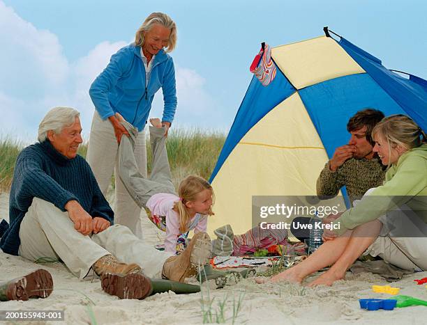 three generational family relaxing on beach by windbreak - beach shelter stockfoto's en -beelden