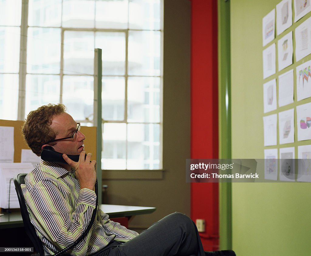 Businessman talking on phone, looking at charts hanging on wall