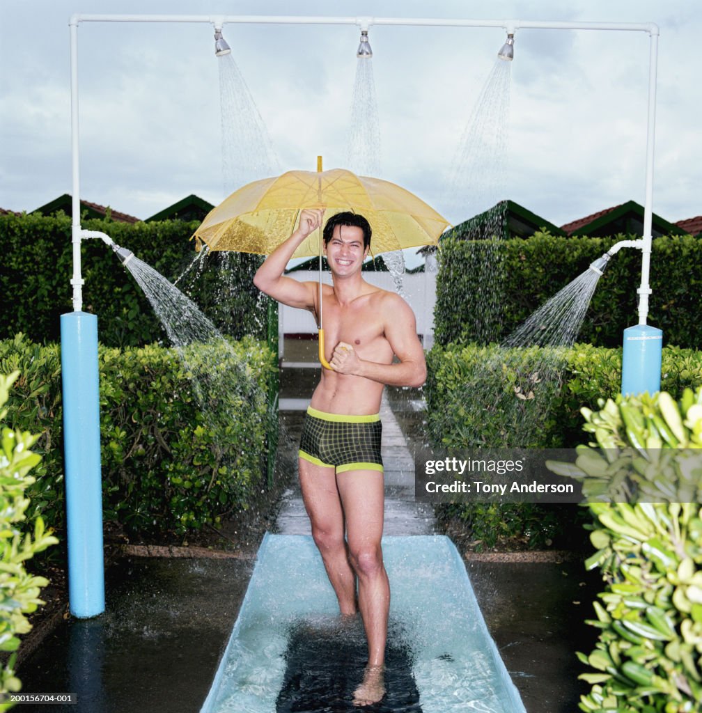 Young man standing under umbrella under outdoor shower, portrait