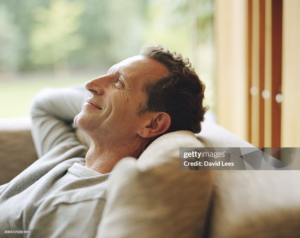 Mature man relaxing on sofa, hands behind head, smiling, profile