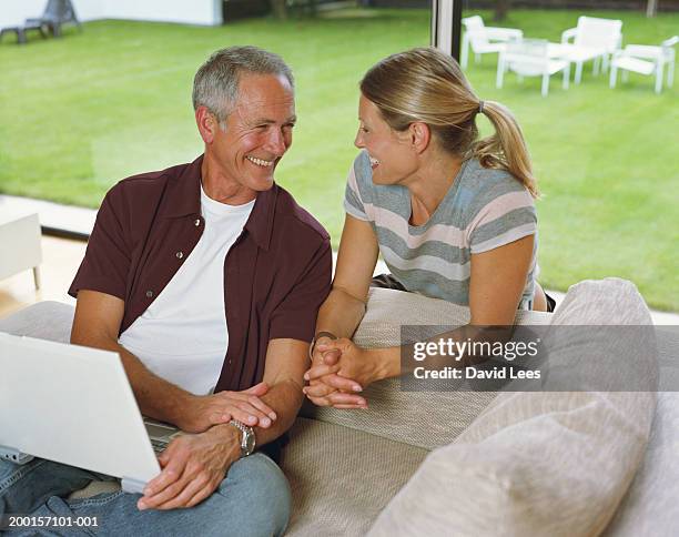 mature couple on sofa laughing, lap top computer on man's lap - woman sitting top man stock pictures, royalty-free photos & images